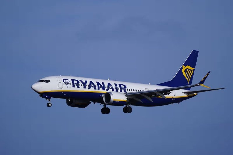A Ryanair Boeing 737 commercial jetliner descends with its landing gear deployed against a hazy blue sky.
