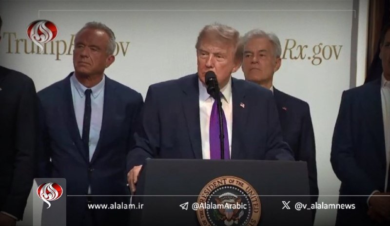 A man in a dark suit and purple tie speaks at a podium bearing the Presidential Seal, flanked by several other men in suits before a backdrop displaying "TrumpRx.gov."