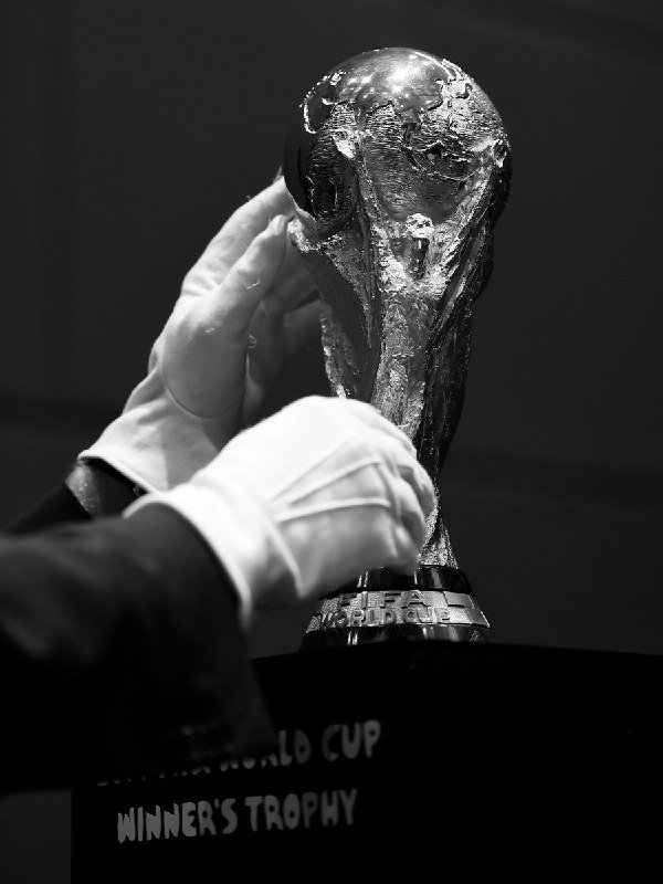 White-gloved hands polish a gold trophy atop a black pedestal labeled "WINNER'S TROPHY" and "WORLD CUP."