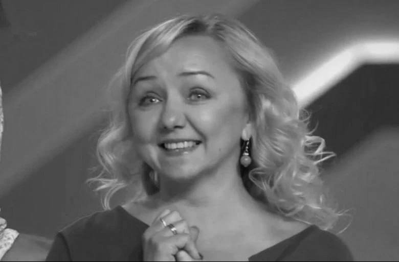 A smiling blonde woman wearing a dark dress and pearl drop earrings looks off-camera in this black-and-white photograph.