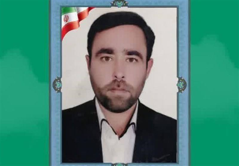 A framed portrait photograph of a bearded man in a dark suit and white shirt, with an Iranian flag graphic displayed in the upper left corner.