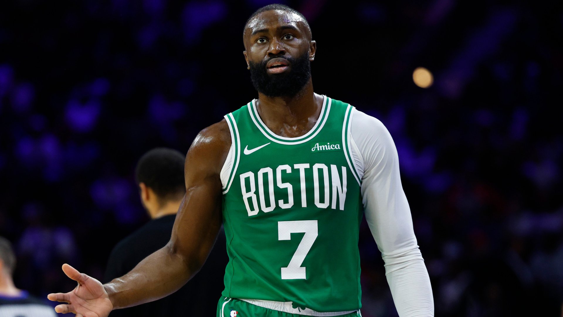 A basketball player wearing a green Boston jersey with the number 7 stands on a court, gesturing with his right hand during a game.