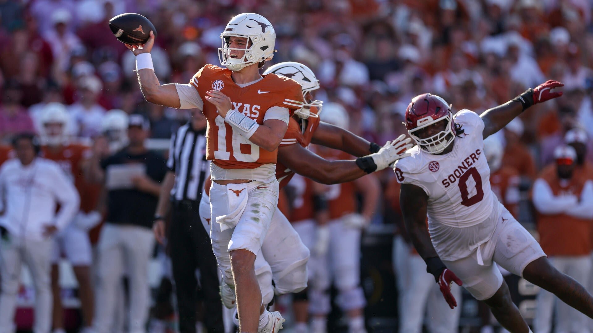 A Texas football quarterback wearing jersey number 16 throws a pass while being pressured by two Oklahoma defenders in white jerseys during a daytime game.