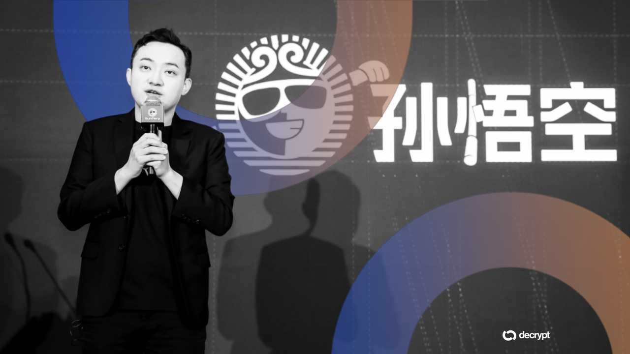 A man in a black suit speaks into a microphone at a Decrypt event, standing before a backdrop displaying a cartoon monkey logo and Chinese characters.