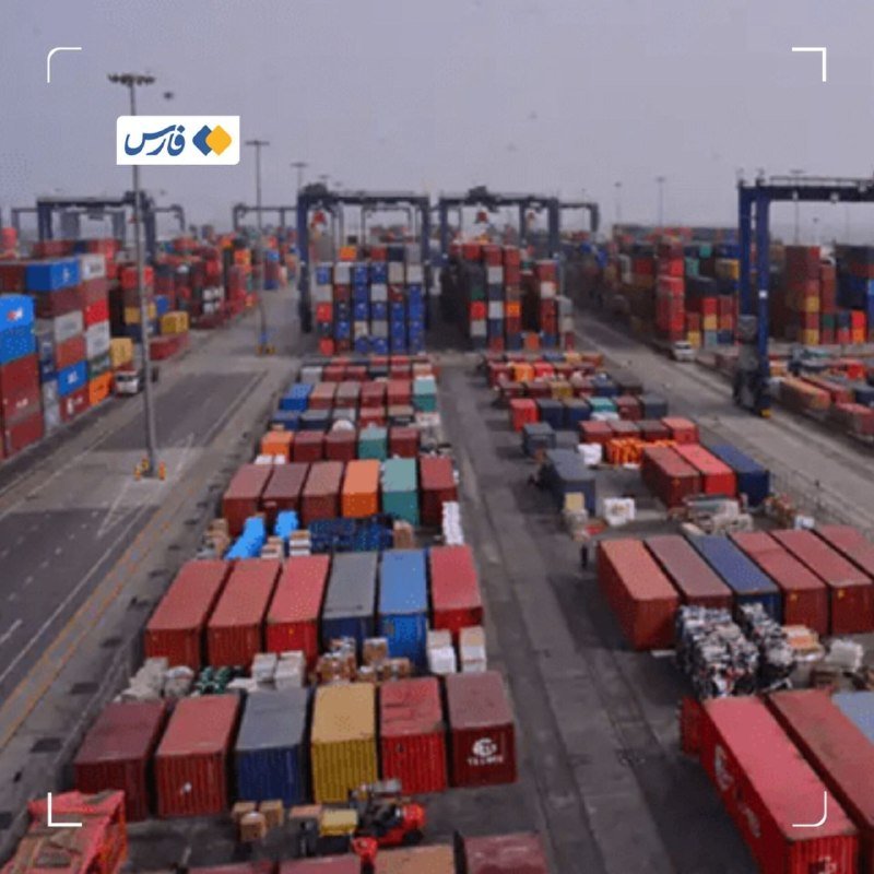 Rows of multicolored shipping containers are stacked in an outdoor port terminal, with gantry cranes visible in the background beneath a hazy sky.