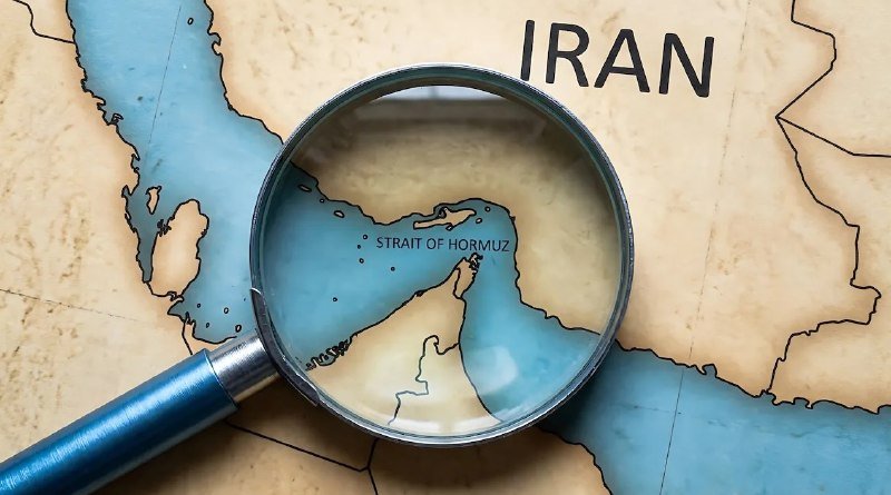 A blue-handled magnifying glass rests on a map, enlarging the "Strait of Hormuz" label near the word "IRAN."