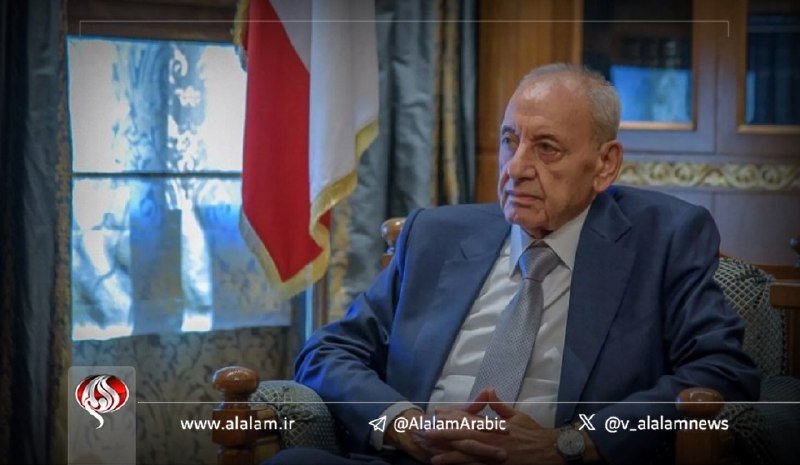 An older man in a blue suit and tie sits in an ornate chair beside a flag, with an Al-Alam news watermark visible at the bottom.