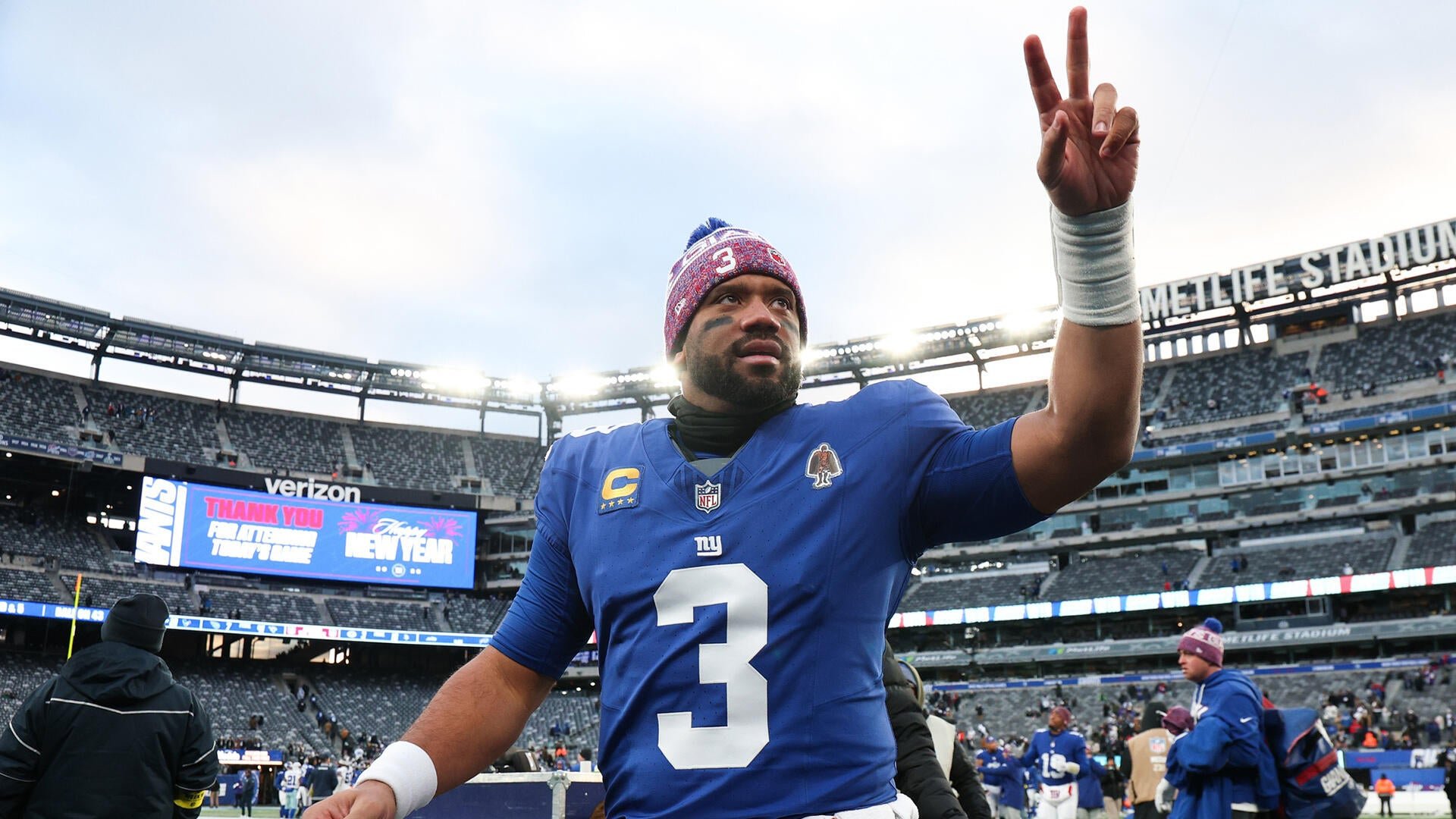 A New York Giants football player wearing jersey number 3 and a winter beanie raises two fingers toward the crowd at MetLife Stadium, with a scoreboard reading "Thank You Fans, Happy New Year."