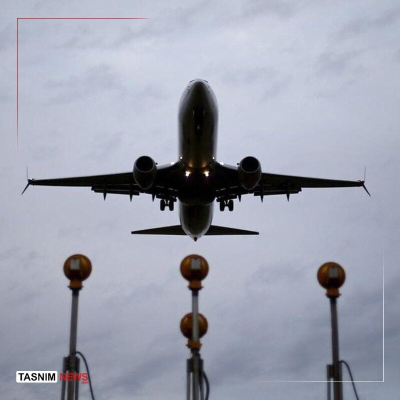 A commercial jetliner ascends into a cloudy sky, viewed head-on from below as it climbs past runway approach lights.
