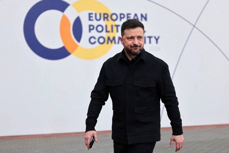 A bearded man in a black jacket walks forward in front of a wall displaying the "European Political Community" logo and text.