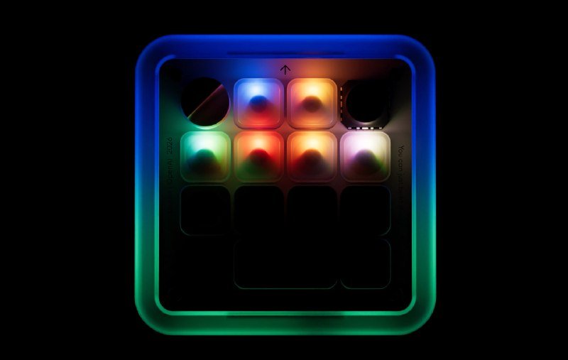 A glowing, square electronic device with a colorful illuminated grid of buttons sits against a black background.