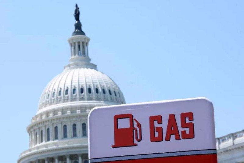 A red and white "GAS" sign with a fuel pump icon stands in the foreground, with the white domed U.S. Capitol building visible behind it against a clear blue sky.