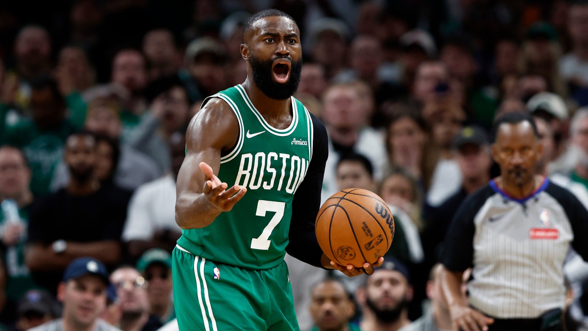 Boston Celtics player wearing jersey number 7 reacts with his mouth open while holding a basketball, with a referee and crowd visible in the background.