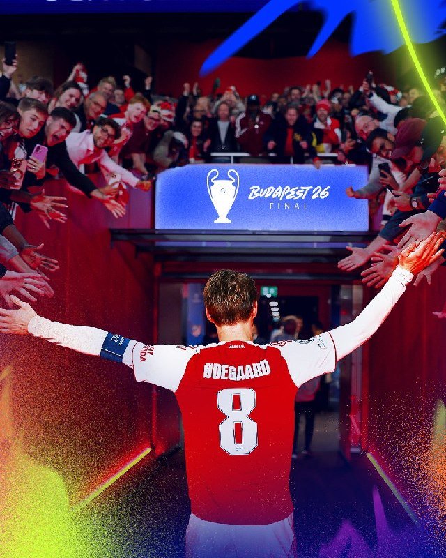 A soccer player wearing a red jersey with "ODEGAARD" and the number 8 raises his arms toward cheering fans reaching out from both sides of a tunnel displaying a "BUDAPEST 26 FINAL" sign.