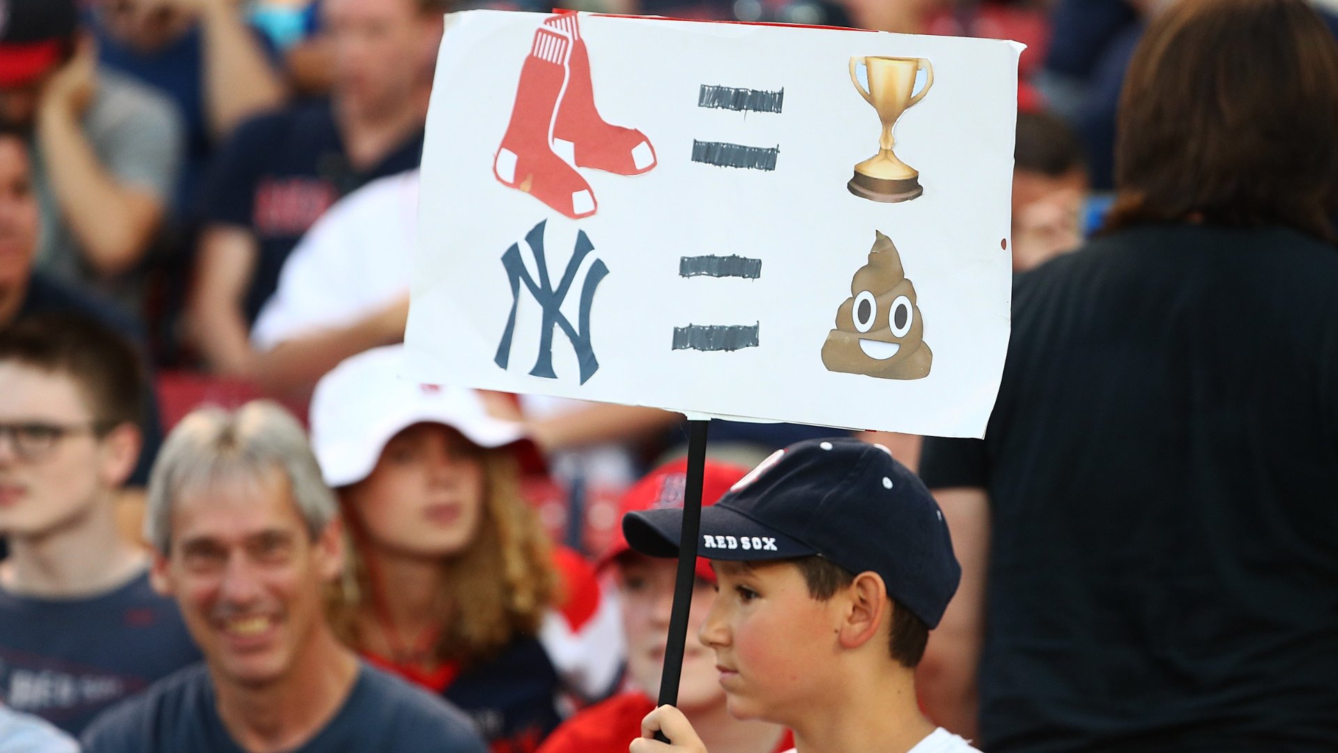 A boy wearing a "Red Sox" cap holds up a sign comparing Red Sox socks, a trophy, the Yankees logo, and a poop emoji with equals signs.