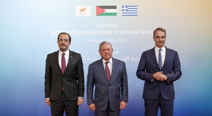 Three men in suits pose together in front of a backdrop displaying the flags of Cyprus, Jordan, and Greece, with text reading "The Fifth Jordan-Cyprus-Greece Trilateral Summit."