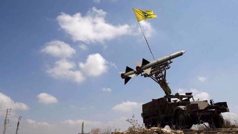 A military vehicle with an elevated surface-to-air missile launcher and a yellow flag stands against a partly cloudy blue sky.