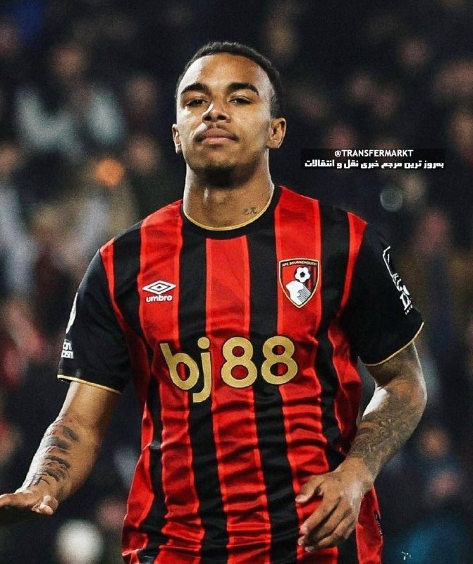 A football player in a red and black striped AFC Bournemouth jersey with "bj88" sponsorship walks against a blurred stadium crowd background.