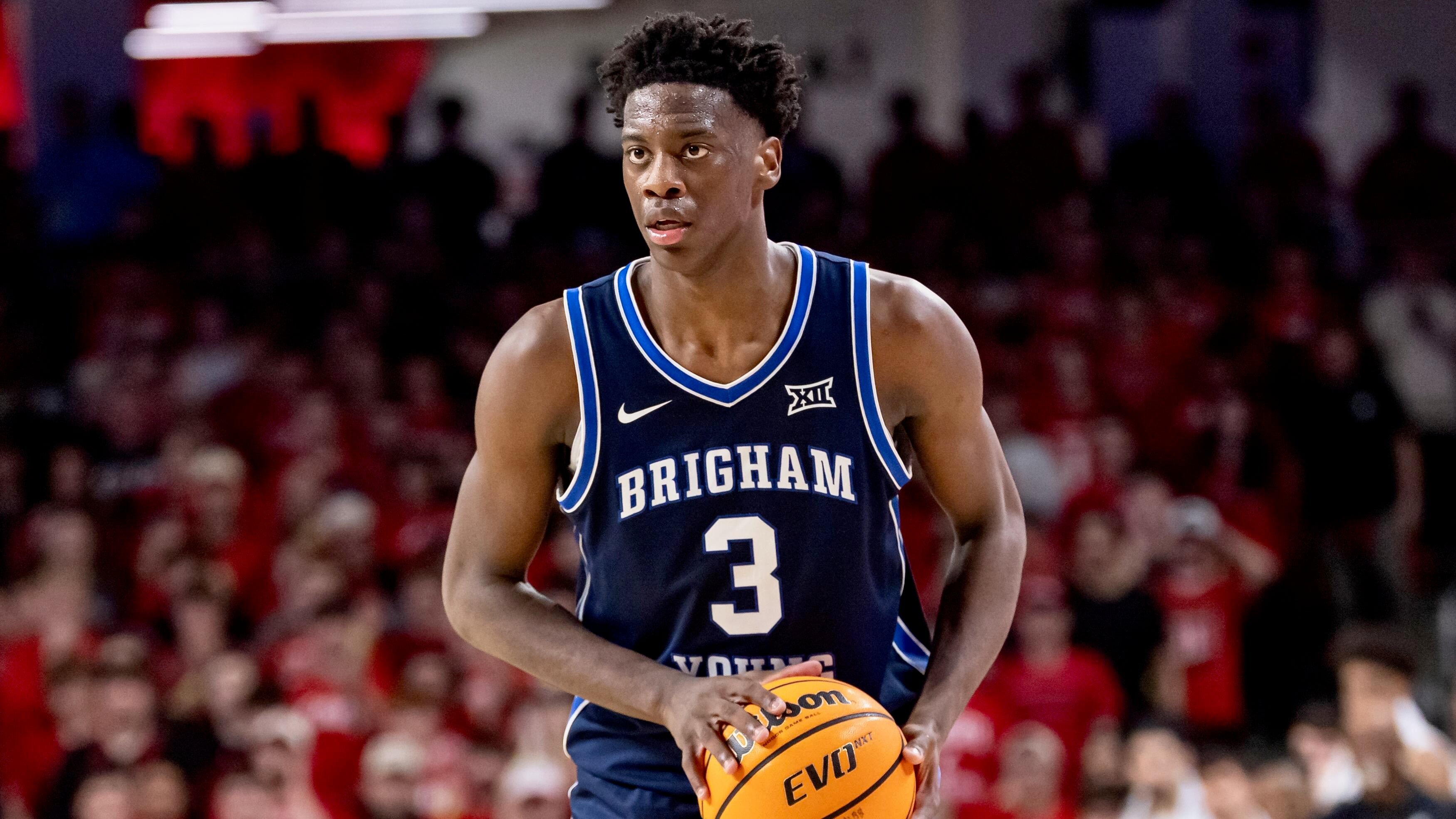 A basketball player in a navy "Brigham" #3 jersey holds a Wilson EVO NXT ball during a game before a crowd wearing red.