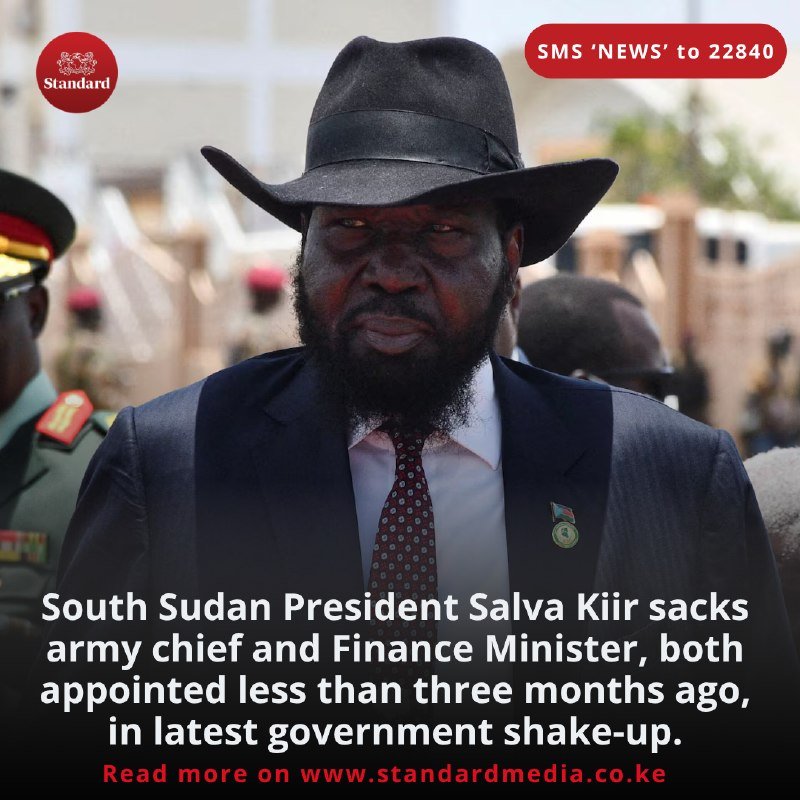 A bearded man in a black cowboy hat and dark suit with a flag pin stands outdoors, with a uniformed officer visible behind him, alongside a Standard news graphic and caption about South Sudan government changes.