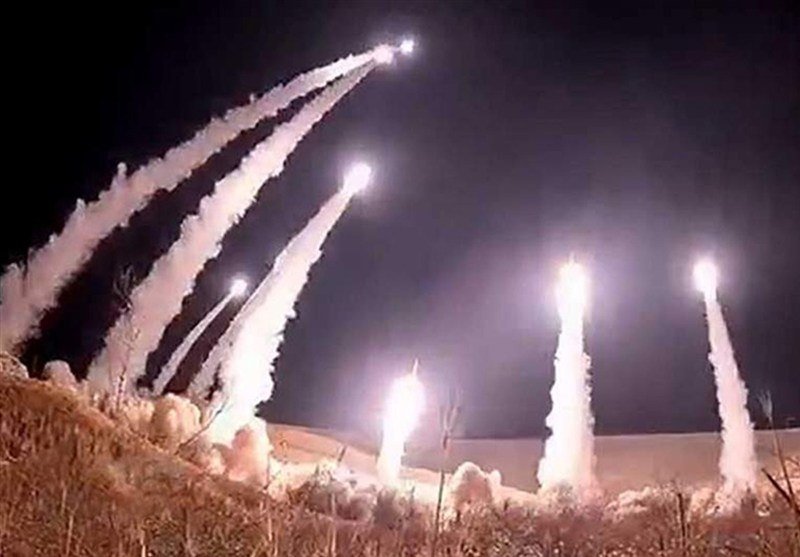 Multiple bright projectiles launch upward at night, leaving glowing smoke trails against a dark sky above a snowy field.
