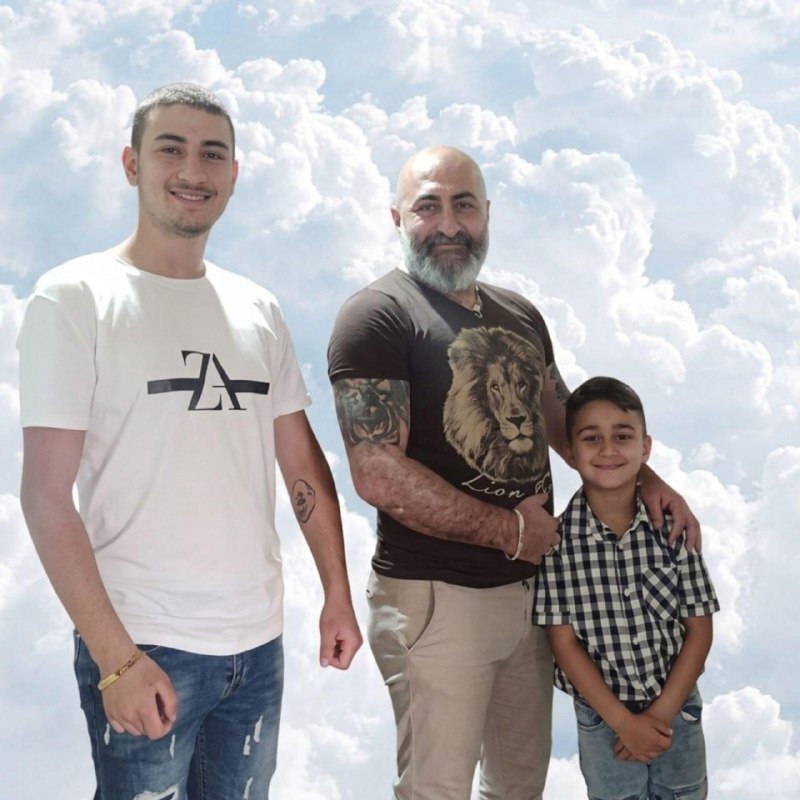 Three people — two males and a boy — pose together against a cloudy sky backdrop.
