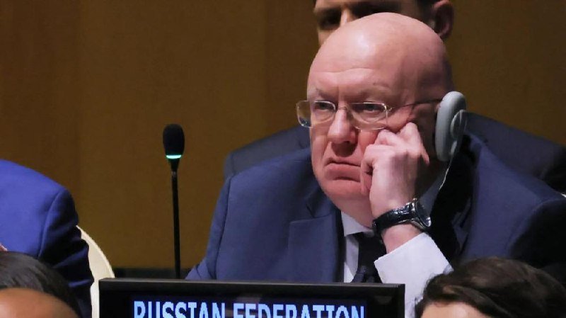 A bald man wearing glasses and a blue suit listens through headphones at a desk labeled "RUSSIAN FEDERATION," with a microphone visible nearby.