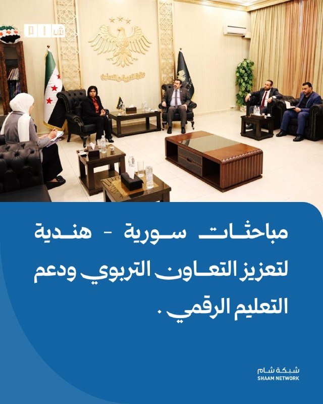 Officials seated in a formal meeting room converse across coffee tables, with an emblem and flags displayed behind them; Arabic text overlays the image.