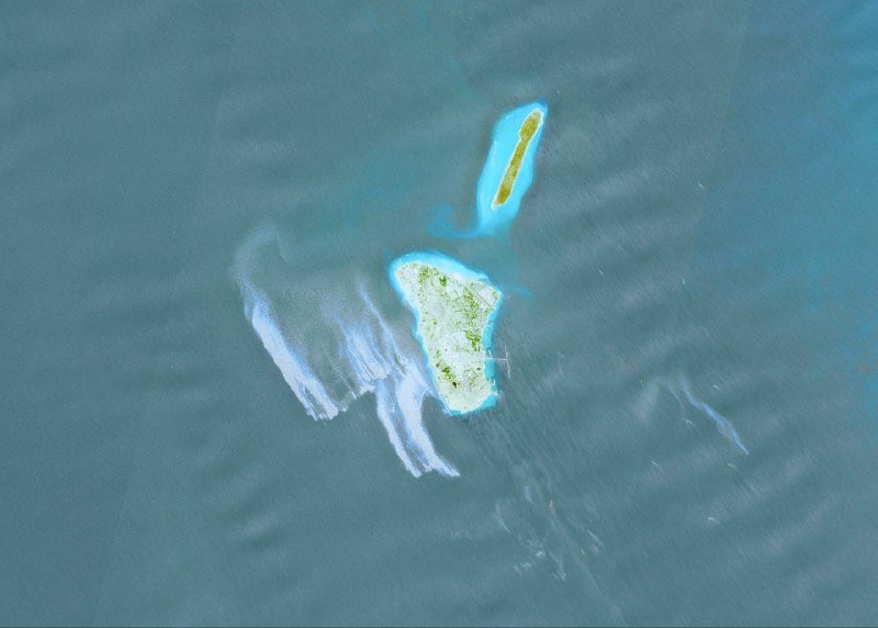 An aerial view shows two small islands surrounded by turquoise waters, with cloud shadows cast across the sea's surface.