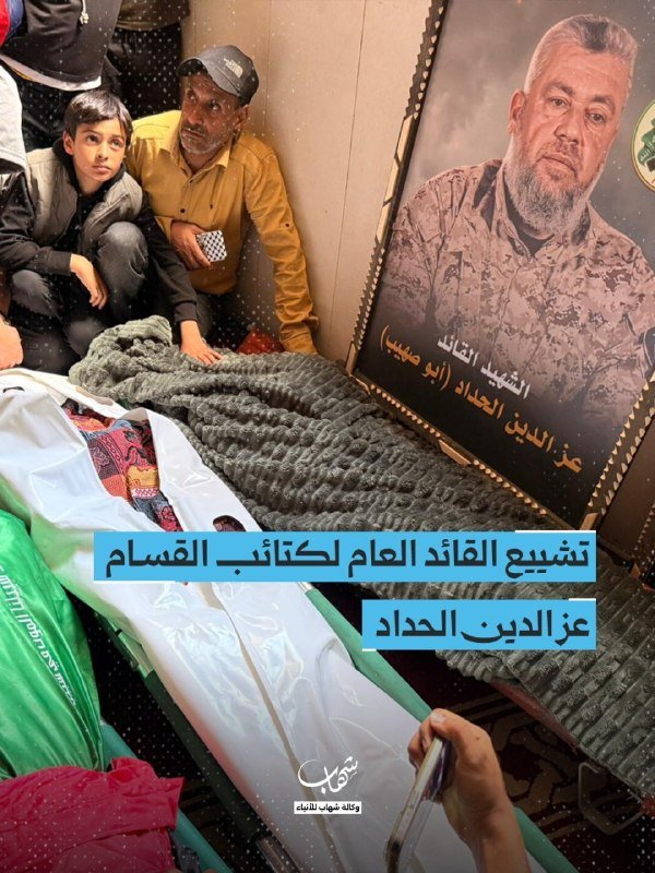 A funeral gathering shows mourners, including a child, seated beside a body wrapped in green and white cloth, next to a framed portrait of a bearded man with Arabic text overlay.