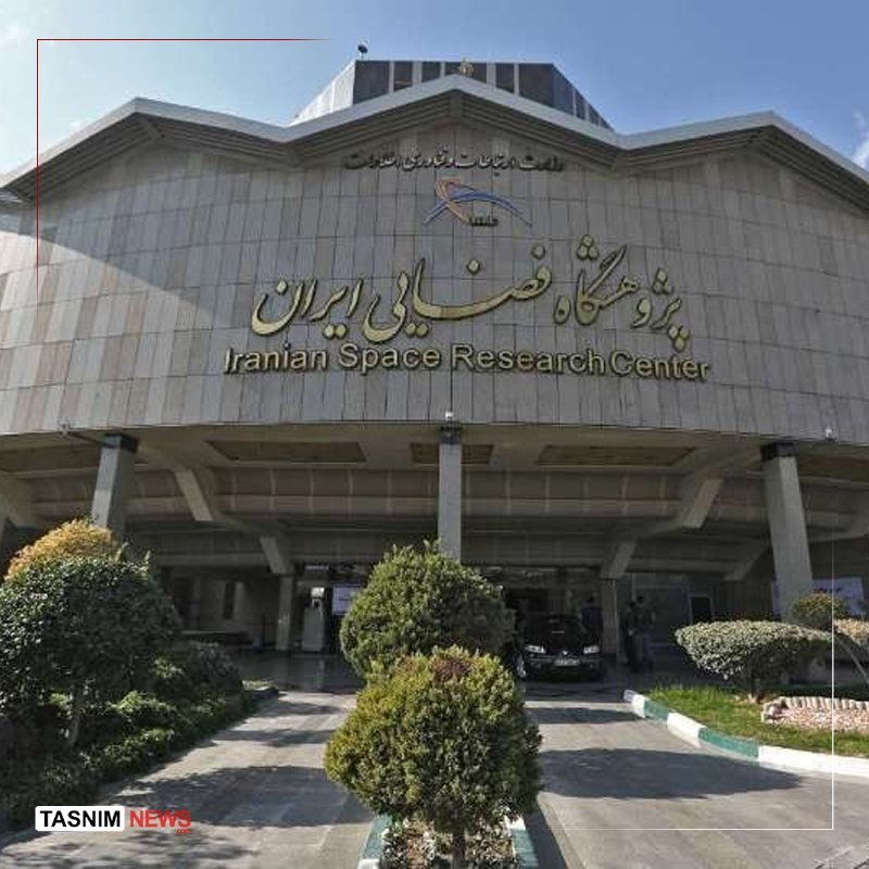 The stone facade of a building displays Persian and English text reading "Iranian Space Research Center," with a parked car and trimmed shrubs at the entrance.
