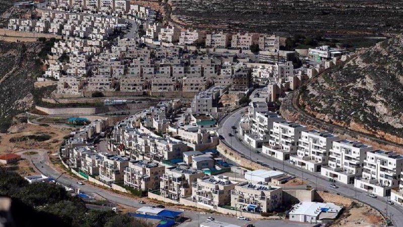 A hillside residential development of densely packed white multi-story buildings winds along curving roads in a rocky, arid landscape.