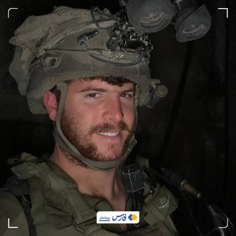 A bearded soldier in tactical gear and a night-vision-equipped helmet smiles inside a dark vehicle.