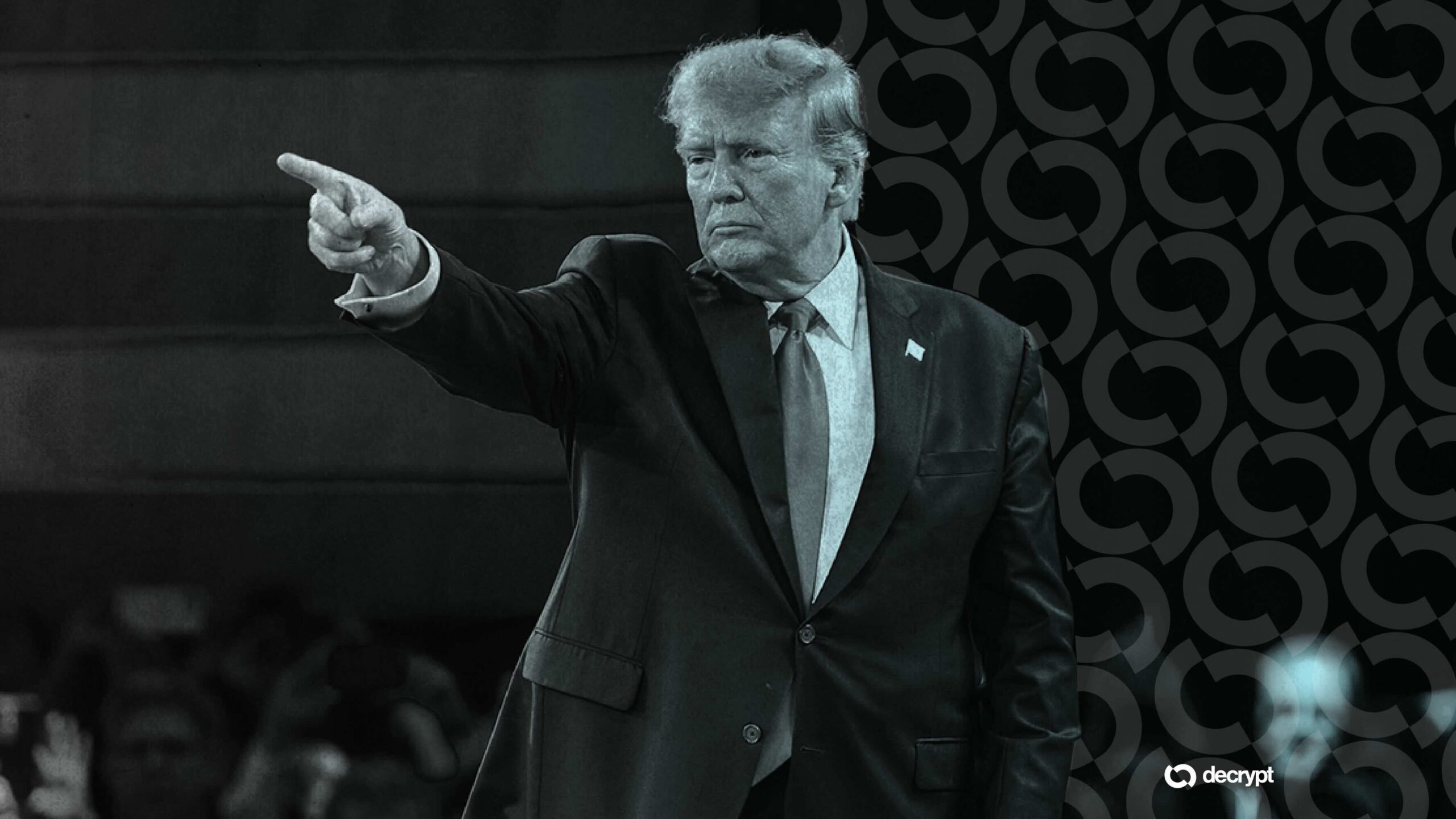 A man with light hair in a dark suit points forward at an event, beside a patterned backdrop with a "decrypt" logo.