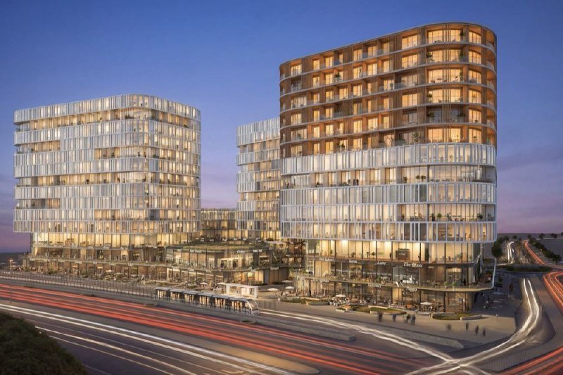 Illuminated modern multi-story buildings with curved facades and lit windows stand beside a busy roadway with streaks of vehicle light trails at dusk.