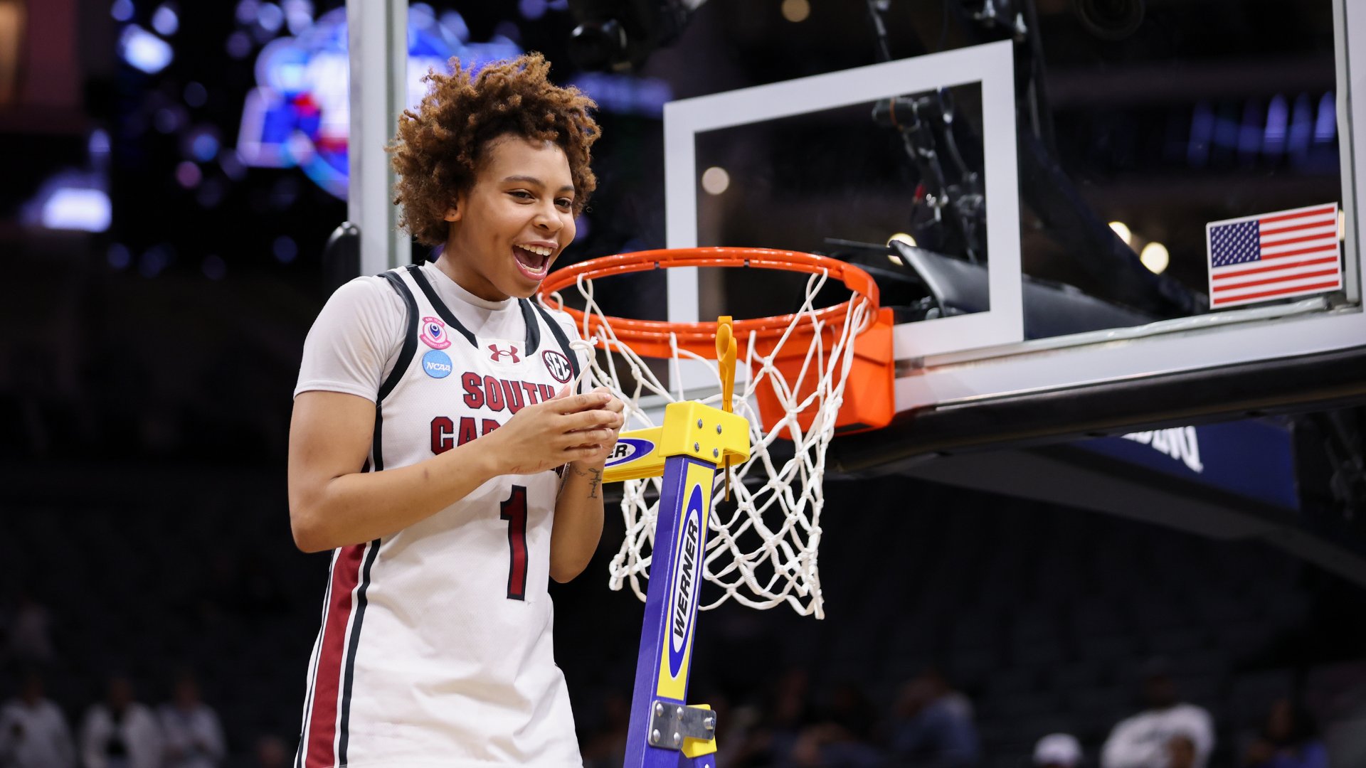 A South Carolina women's basketball player smiles broadly while cutting down the net after a championship win.