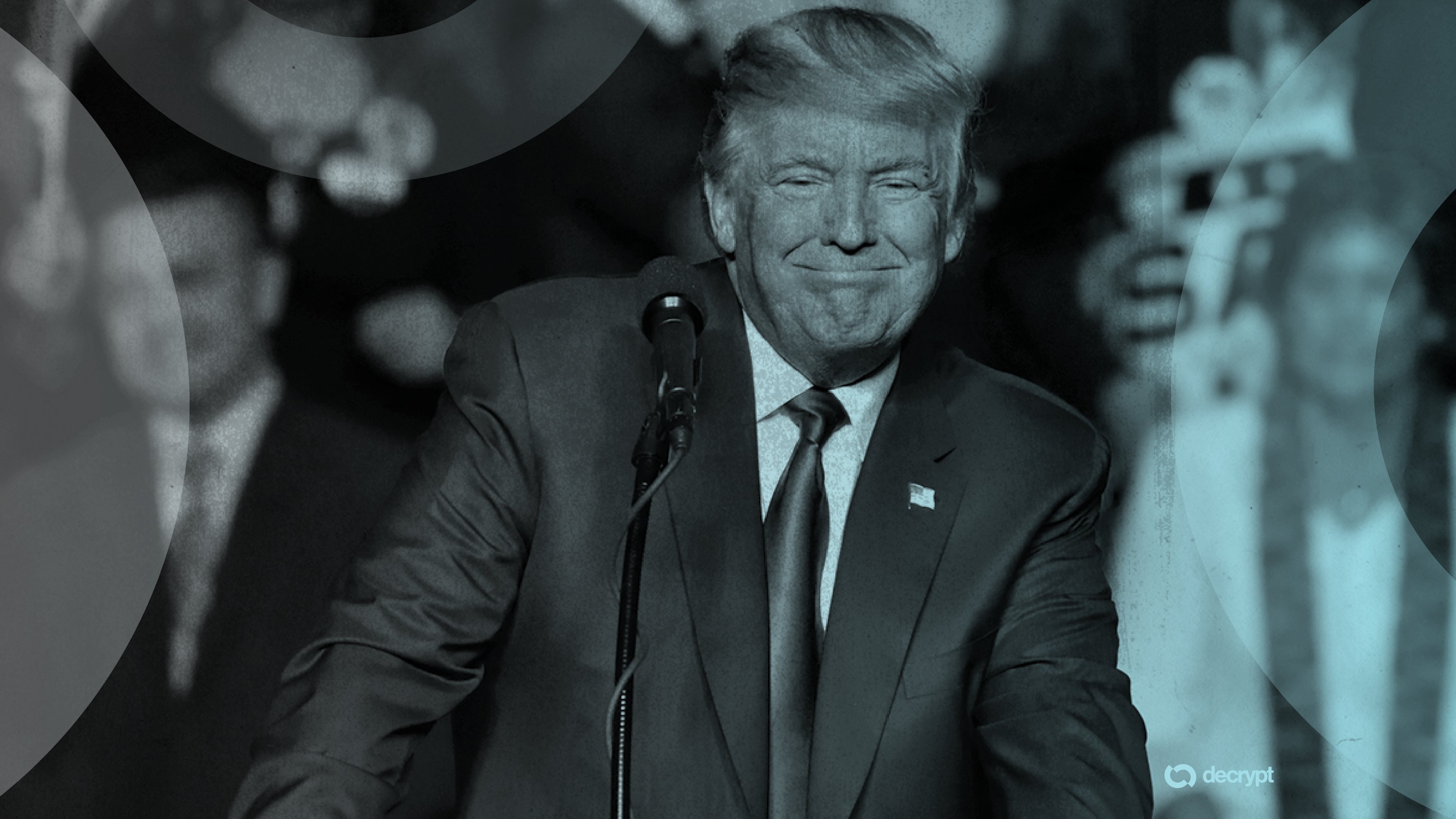 A man in a dark suit and tie stands at a microphone, smiling, with a small flag pin on his lapel; the "decrypt" logo appears in the bottom corner.