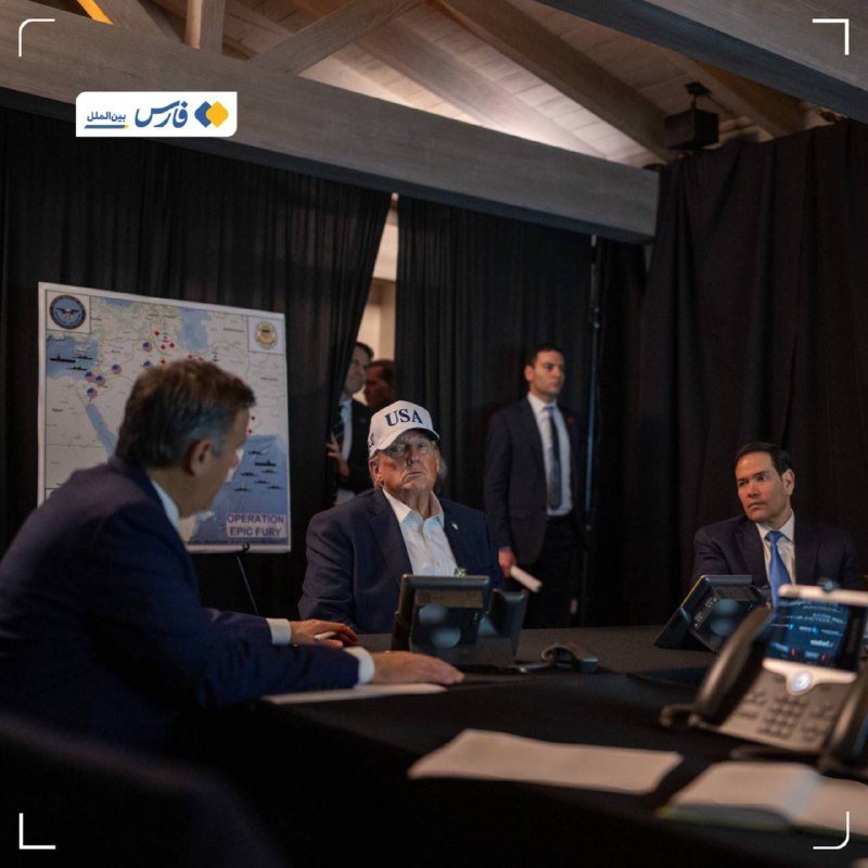 Men in suits sit at a conference table with laptops and a phone, near a map of the Middle East labeled "OPERATION EPIC FURY."