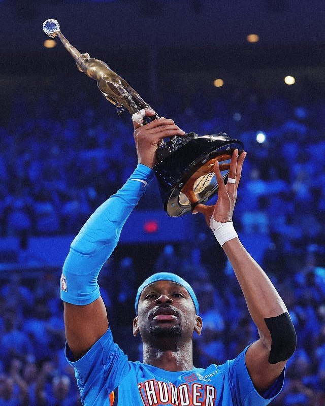 A basketball player in a blue "Thunder" jersey holds a tall gold statuette trophy above his head in front of a crowded arena.