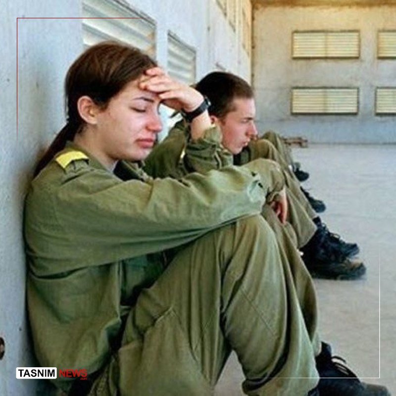 Several people in olive-green uniforms sit against a concrete wall with their eyes closed, one resting their hand on their forehead, with a "Tasnim News" watermark visible.