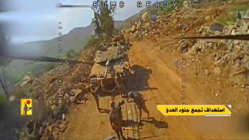 A military vehicle navigates a rocky mountain road with soldiers on foot, shown through a targeting reticle with "BOMB READY" text displayed above.