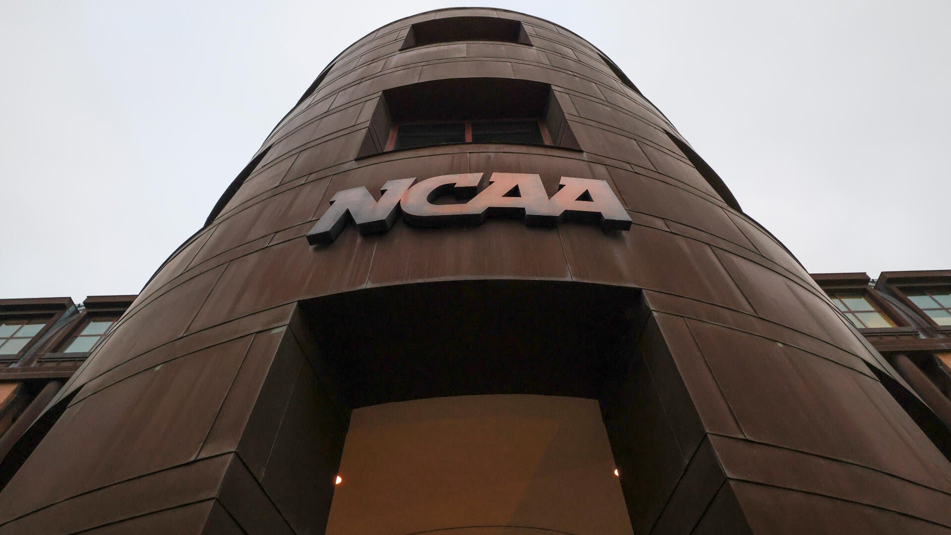 A low-angle view shows a curved, brown-paneled building facade featuring a metallic NCAA logo above a recessed entrance.