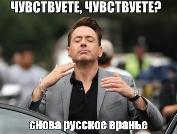 A man in a gray blazer closes his eyes and raises both hands while standing outdoors, with blurred figures and a vehicle in the background; Russian text appears above and below.