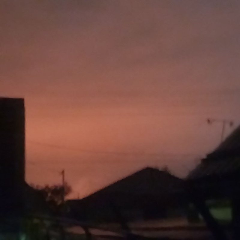 A pink and orange sunset sky fills the frame above silhouetted rooftops, power lines, and distant hills.