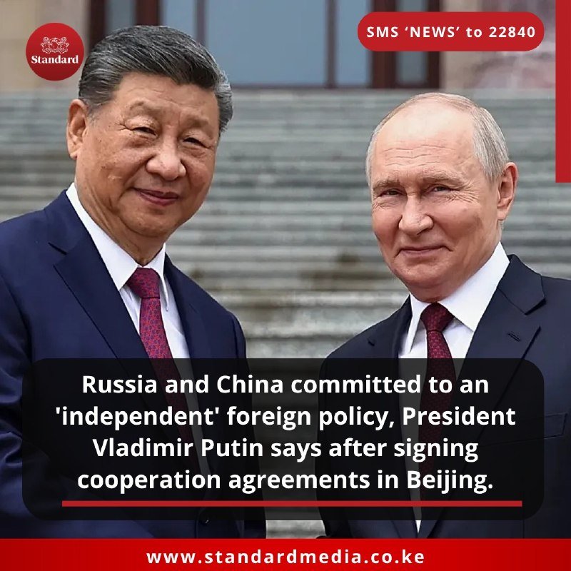 Two men in dark suits and red ties stand side by side smiling on stone steps, overlaid with a news caption about Russia-China cooperation agreements in Beijing.