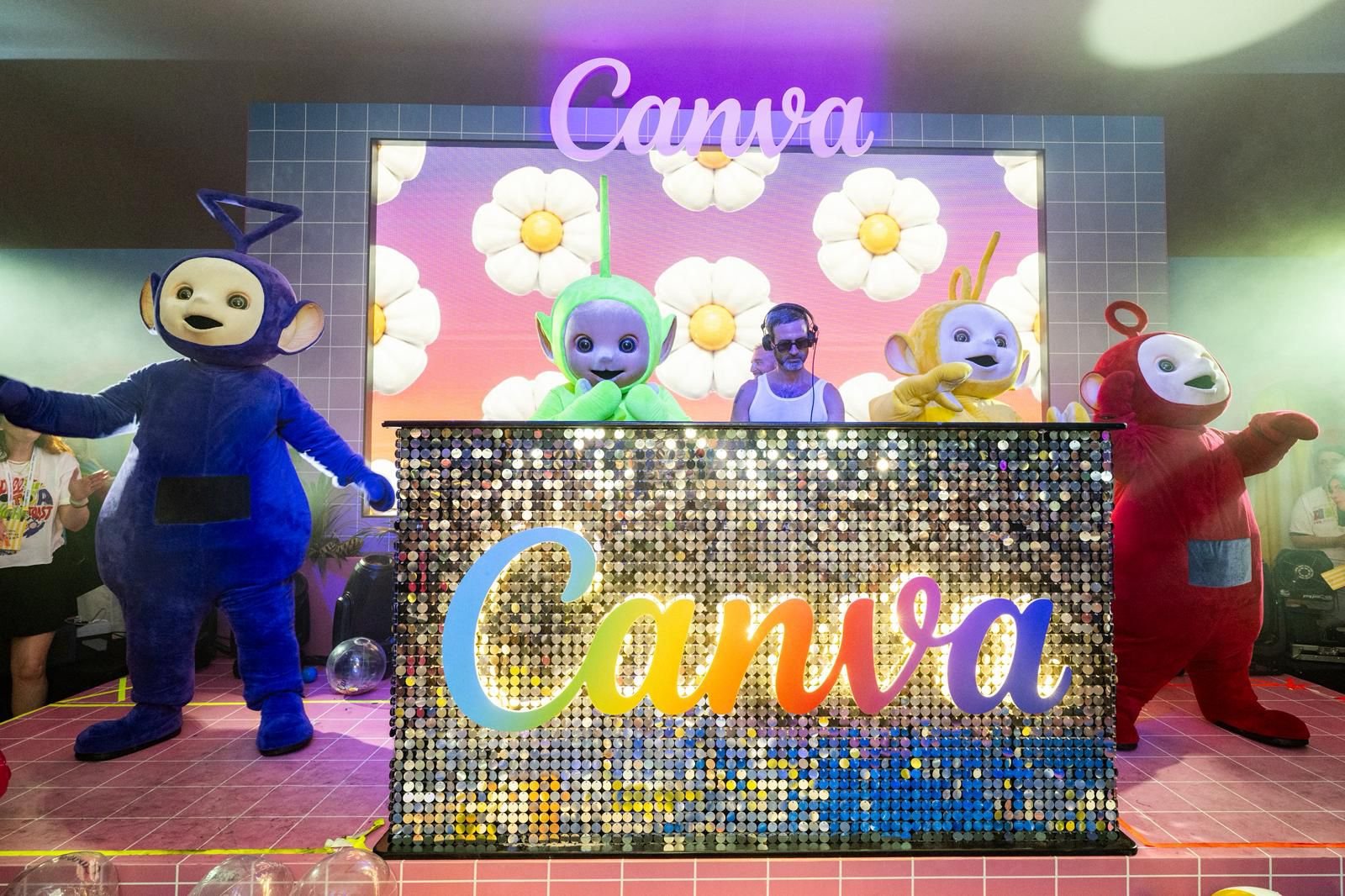 Costumed Teletubbies characters and a DJ perform on a stage featuring a sequined "Canva" logo and a floral-lit backdrop.