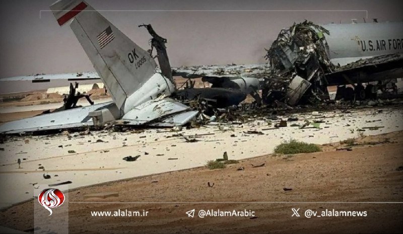 Wreckage of a U.S. Air Force aircraft lies scattered across a sandy surface, with its torn tail section displaying an American flag and debris spread widely.