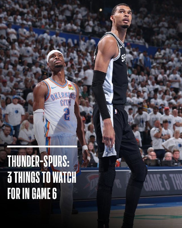 Two basketball players, one in an Oklahoma City jersey and another in a black jersey, stand on the court looking upward during a game before a crowd.