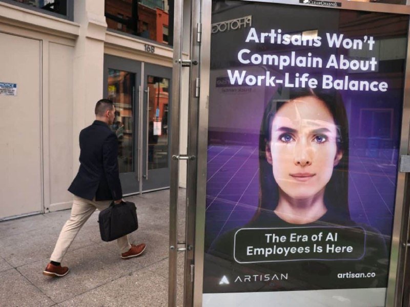 A man in a blazer carrying a briefcase walks past a street-side digital advertisement reading "Artisans Won't Complain About Work-Life Balance: The Era of AI Employees Is Here" by artisan.co.