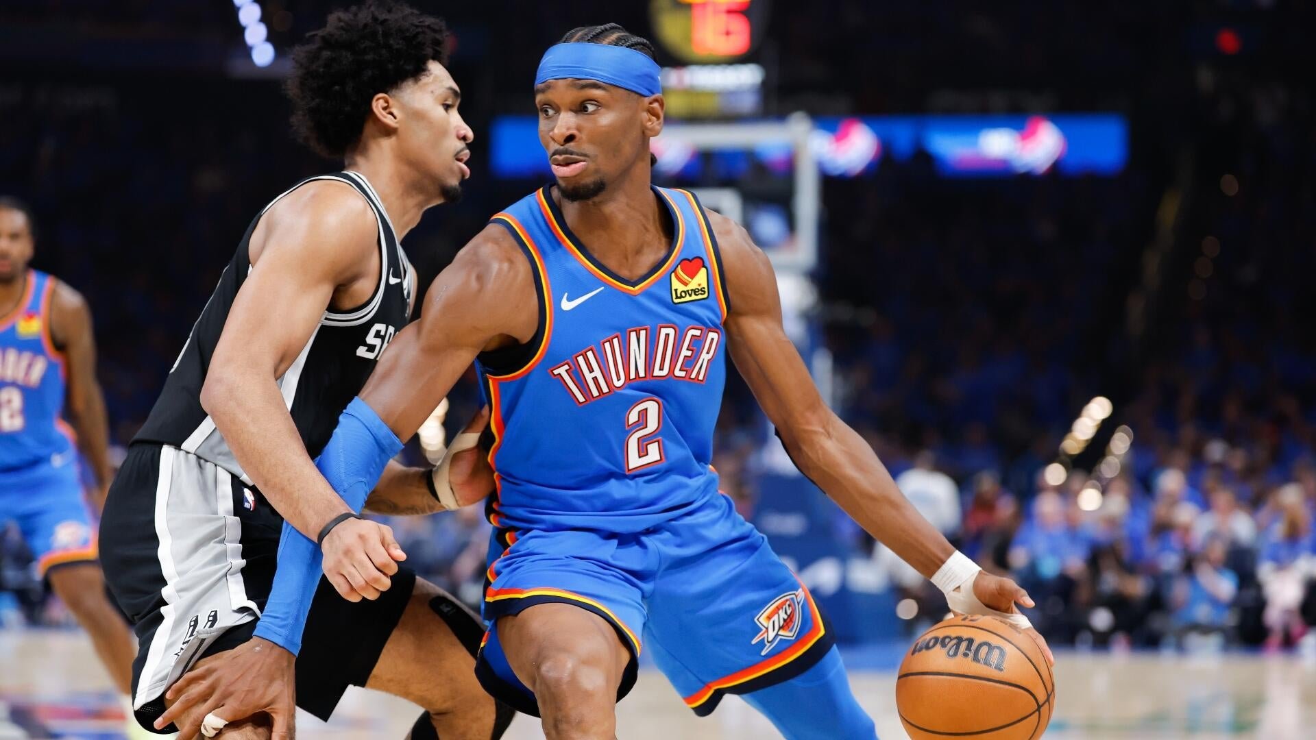Oklahoma City Thunder player #2 in a blue jersey dribbles the basketball while being defended by a player in a black jersey during an NBA game.